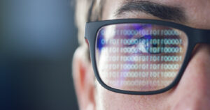A man looking at a computer monitor reflectin into his eyeglasses